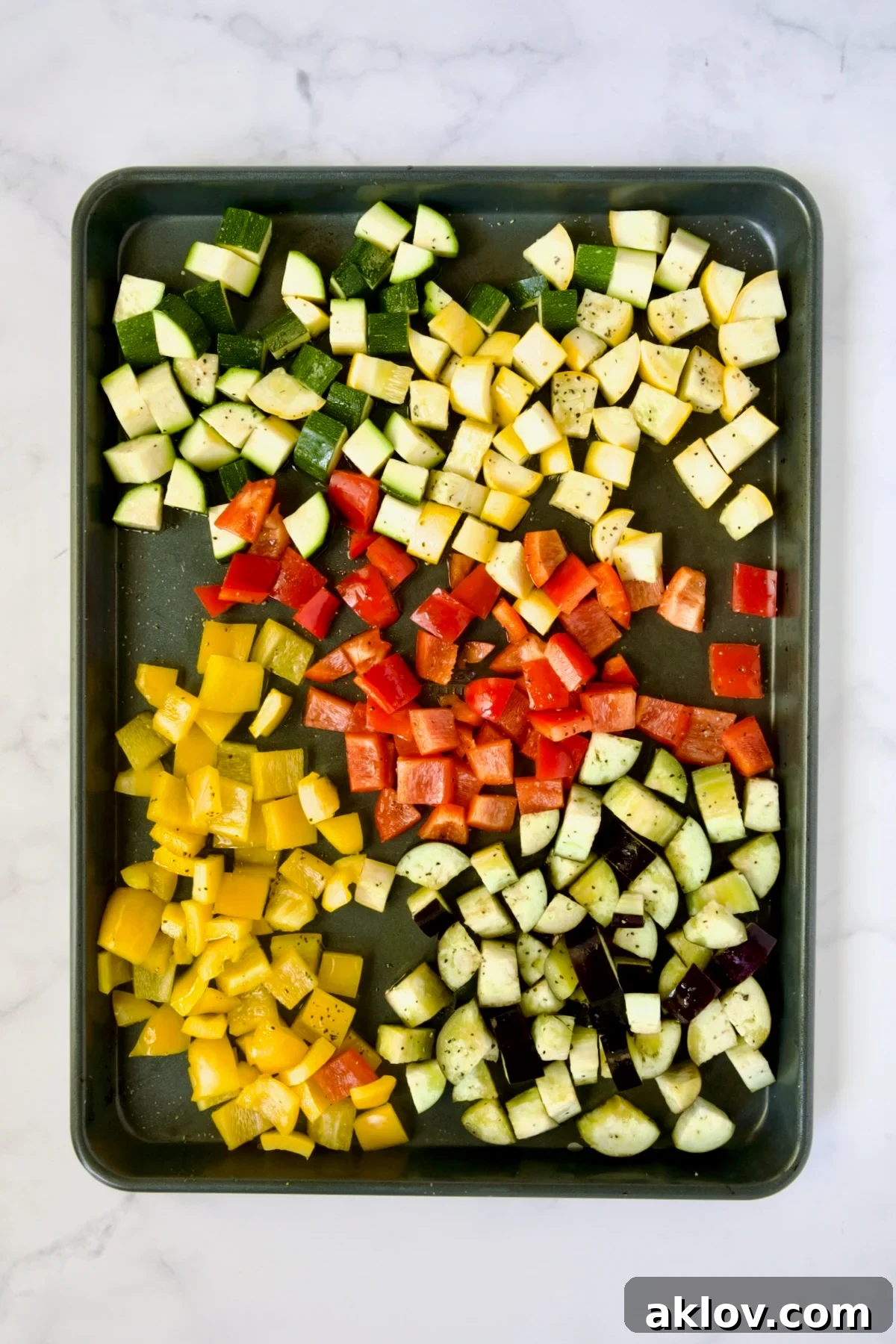 Cubed zucchini, yellow squash, eggplant, yellow and red bell pepper on rimmed sheet pan before being roasted.