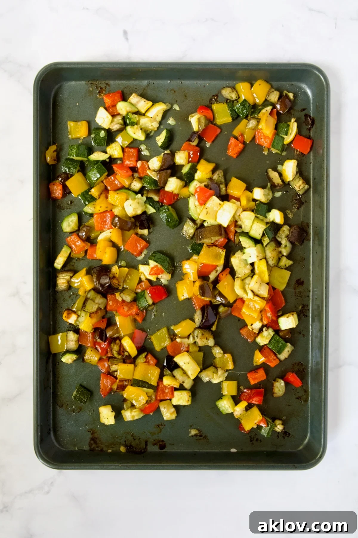 Cubed zucchini, yellow squash, eggplant, yellow and red bell pepper on rimmed sheet pan after being roasted.