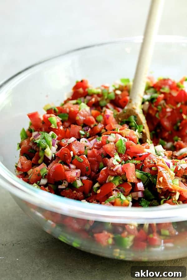 Photo of Salsa Fresca being stirred with wooden spoon in glass bowl.