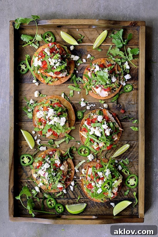 Photo of six Chicken Tostadas with Black Bean Guacamole and Salsa Fresca on wooden tray garnished with cilantro, lime wedges and jalapeno slices.