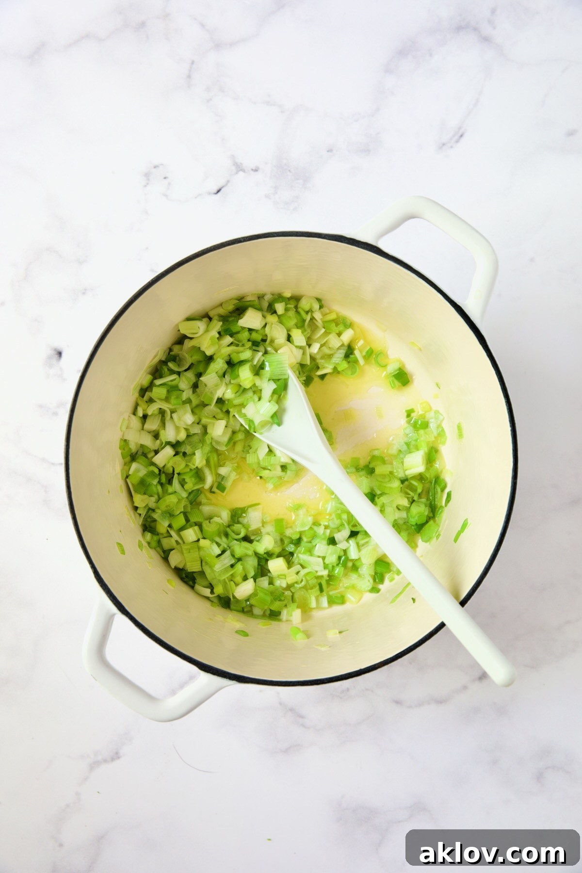 Scallions gently cooking in melted butter and olive oil in a white Dutch oven.