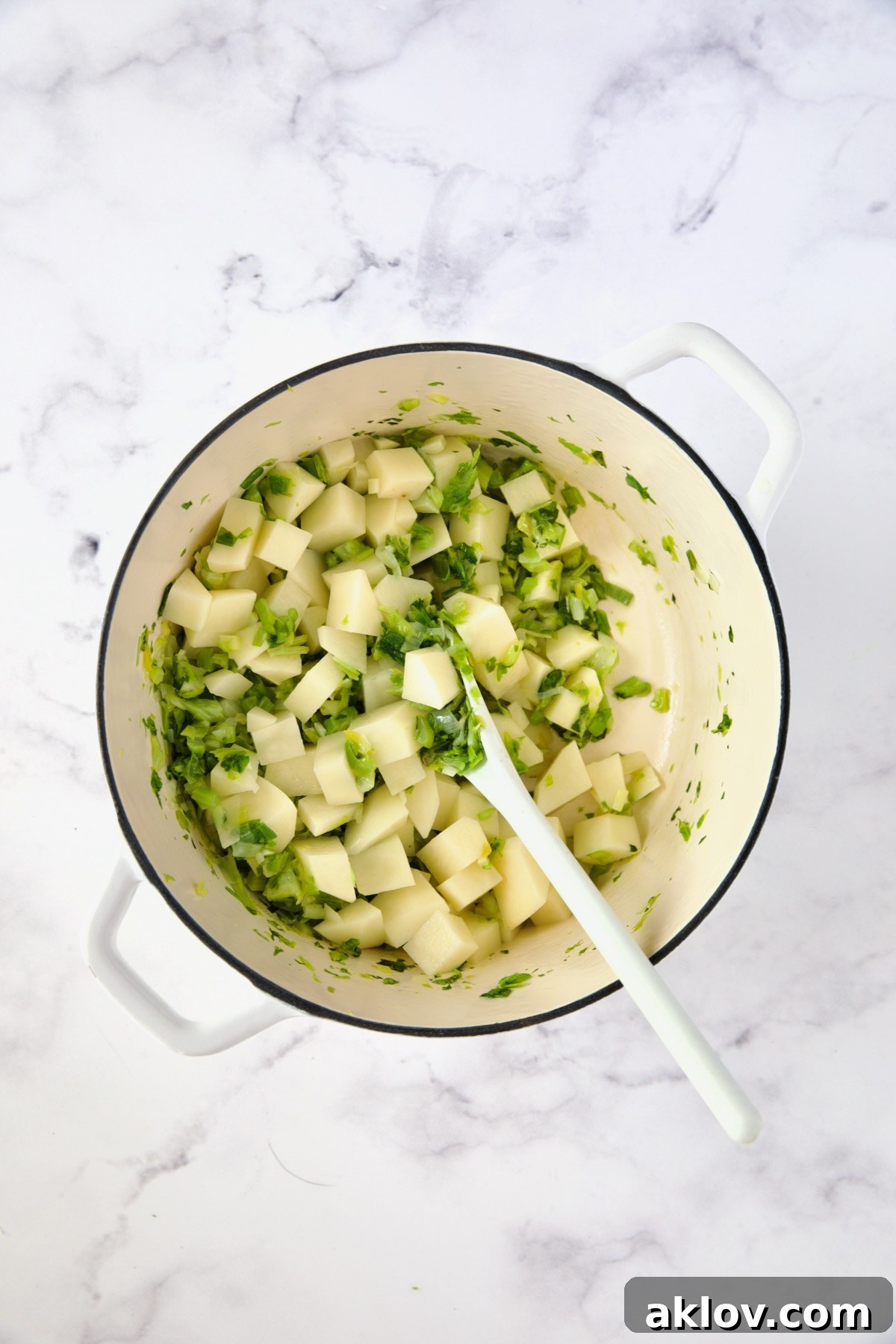 Cubed Russet potatoes added to the sautéed scallions and celery leaves in a white Dutch oven.