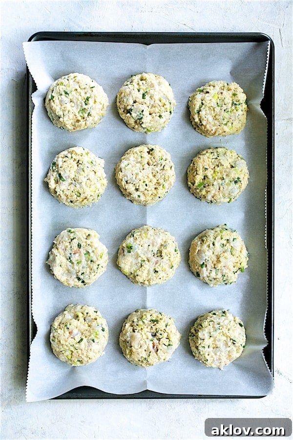 Golden Shrimp Cakes with Fire-Roasted Red Pepper Aioli 4 A batch of uncooked, perfectly formed shrimp cakes arranged neatly on a parchment paper-lined baking sheet, ready for chilling and cooking.