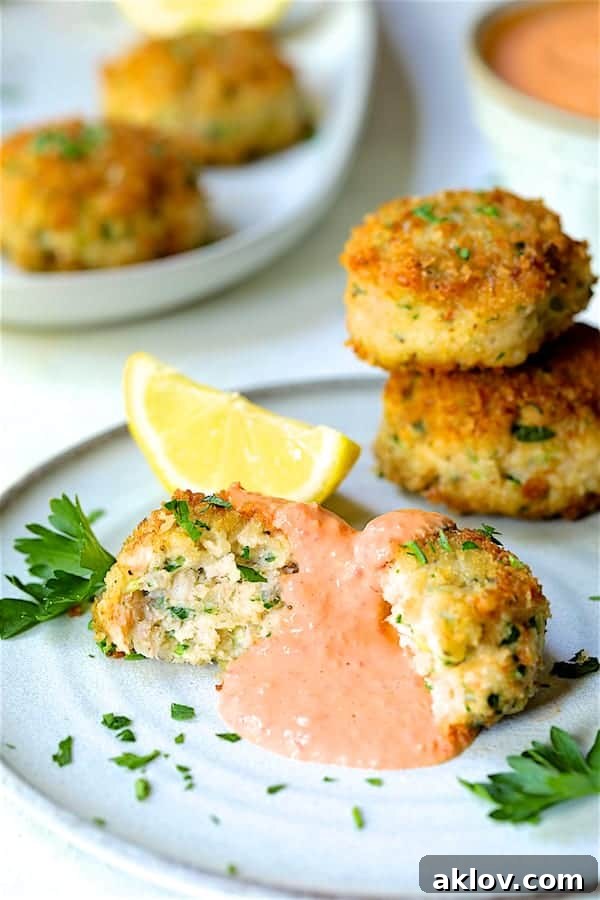 Golden Shrimp Cakes with Fire-Roasted Red Pepper Aioli 10 A close-up view of a single serving of Shrimp Cakes with Roasted Red Bell Pepper Mayonnaise, elegantly presented on a plate with a lemon wedge and parsley garnish.