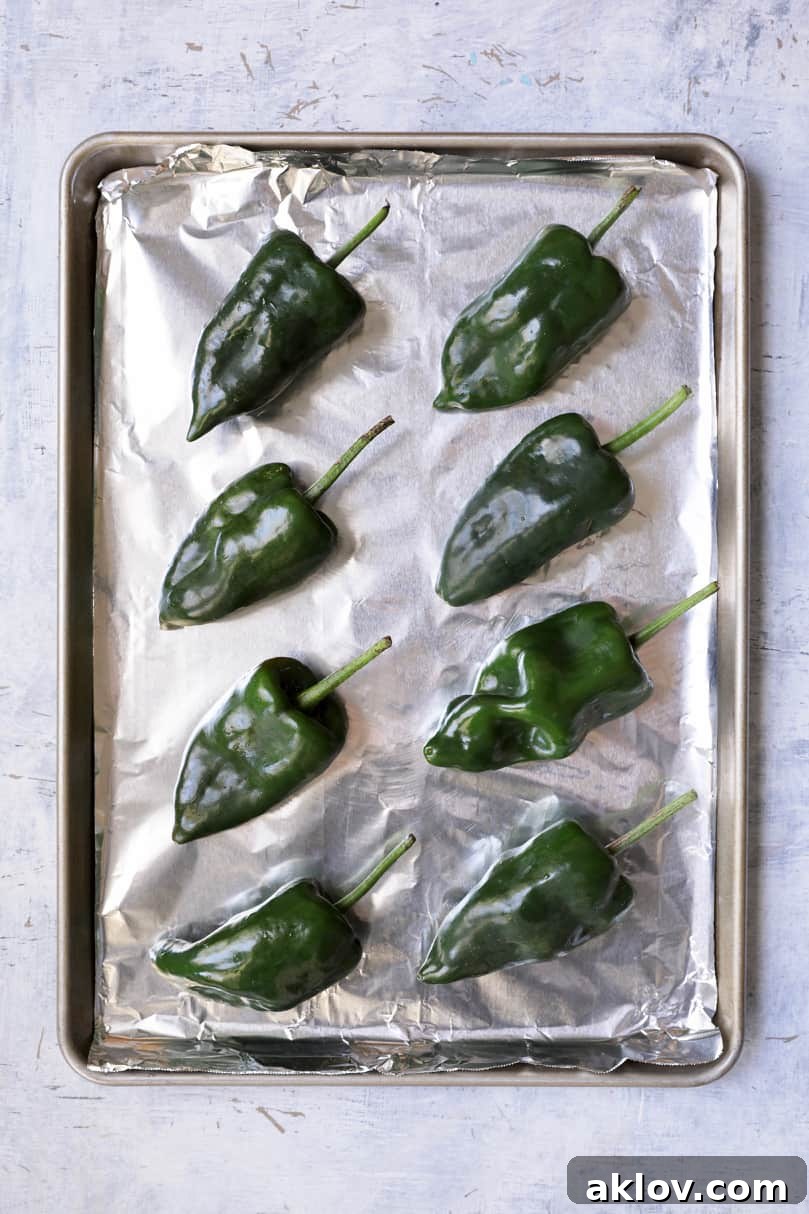 Photo of fresh Poblano peppers neatly arranged on a foil-lined baking sheet, prepared for roasting under the broiler.