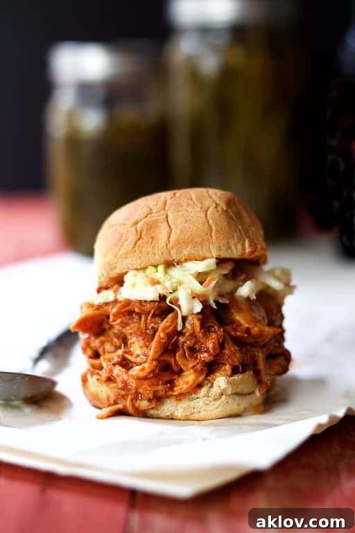 Barbecue chicken sandwich topped with coleslaw on white paper.
