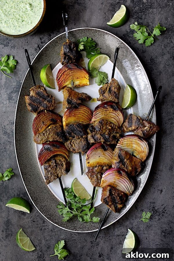 Indian-Style Beef Kabobs with Cilantro-Coconut Sauce - Overhead shot of cooked kabobs on gray-rimmed platter garnished with lime wedges and cilantro