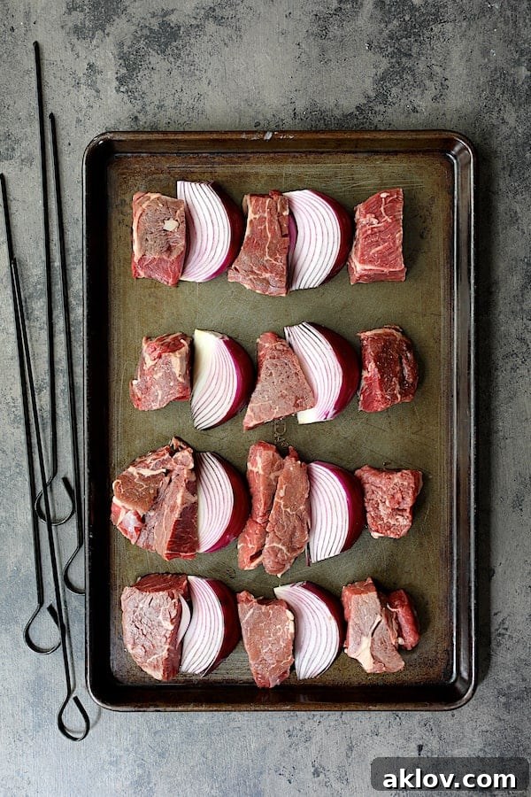 Overhead shot of marinated beef and red onions prepared on a cutting board, ready for threading onto skewers