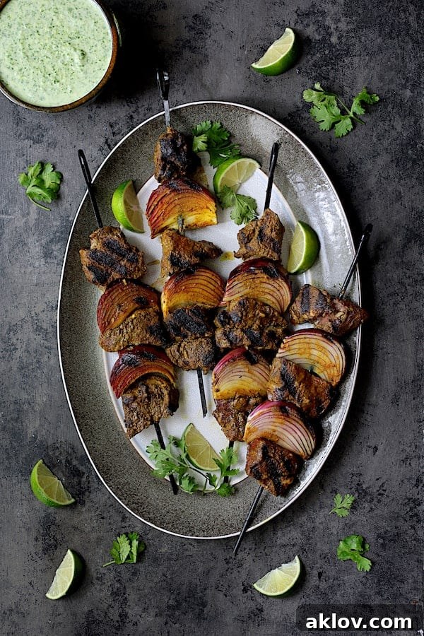 Indian-Style Beef Kabobs with Cilantro-Coconut Sauce on a gray-rimmed platter, garnished with fresh cilantro and lime wedges