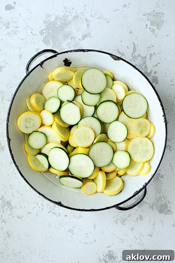 Neatly sliced zucchini and yellow squash rounds in a white colander, prepared for sautéing in a delicious quinoa casserole.