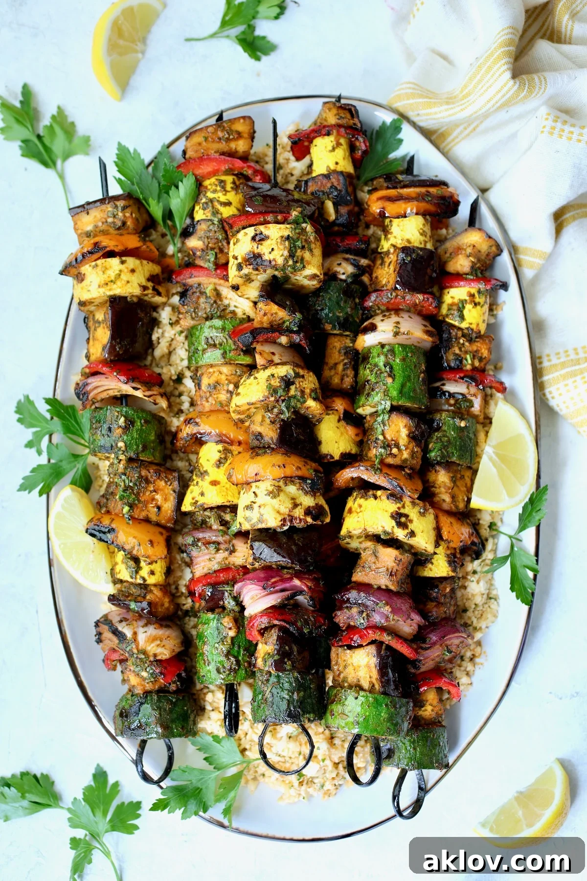 Vibrantly grilled vegetable kabobs arranged on an oval white platter, garnished with fresh parsley and bright lemon slices.