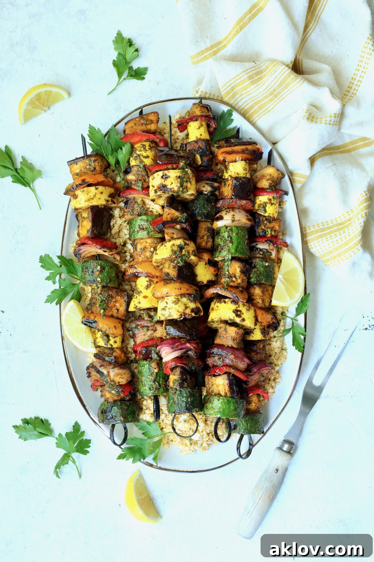 A stunning arrangement of grilled vegetable kabobs presented on an elegant oval white platter, beautifully garnished with fresh parsley and bright lemon slices.