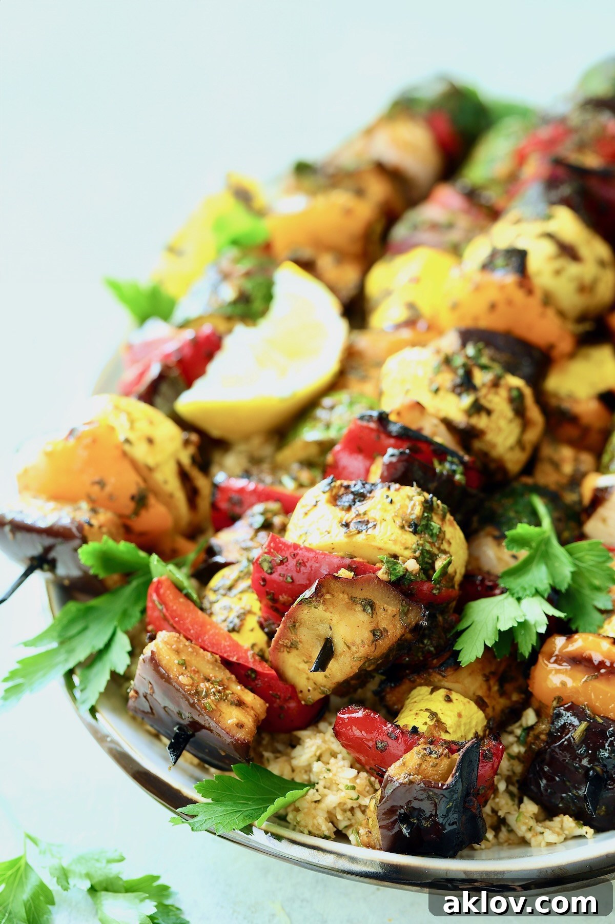 Close-up view of grilled vegetable kabobs on an oval white platter, adorned with green parsley and yellow lemon slices, emphasizing their vibrant colors and smoky char.