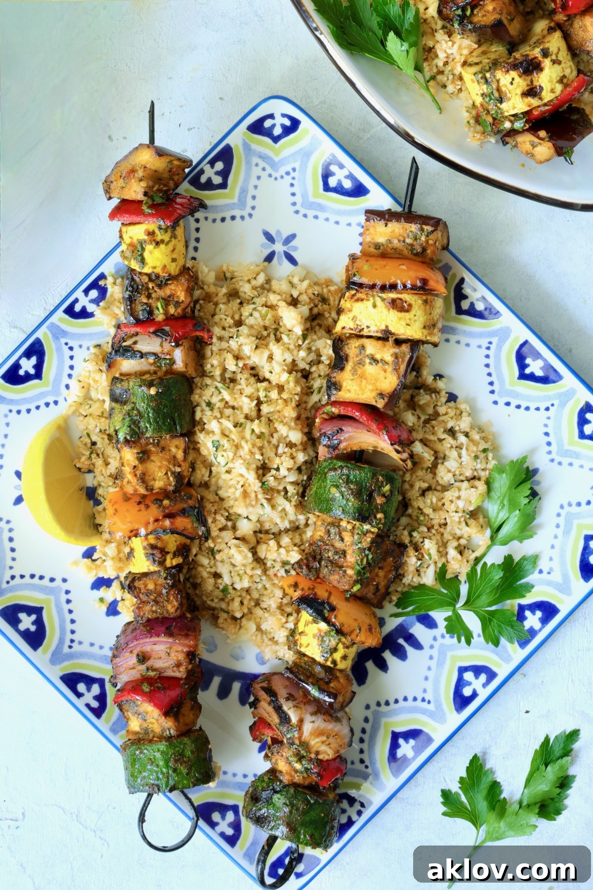 A single portion of grilled vegetable kabobs served on a square plate, garnished with fresh parsley and lemon wedges.