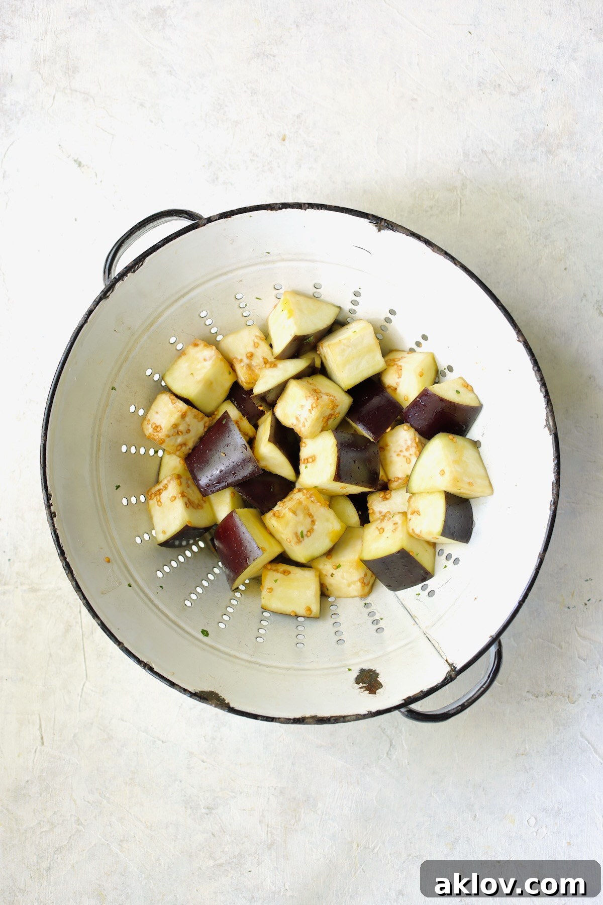 Cubed eggplant, generously salted, draining in a vintage white colander to remove bitterness and excess moisture.