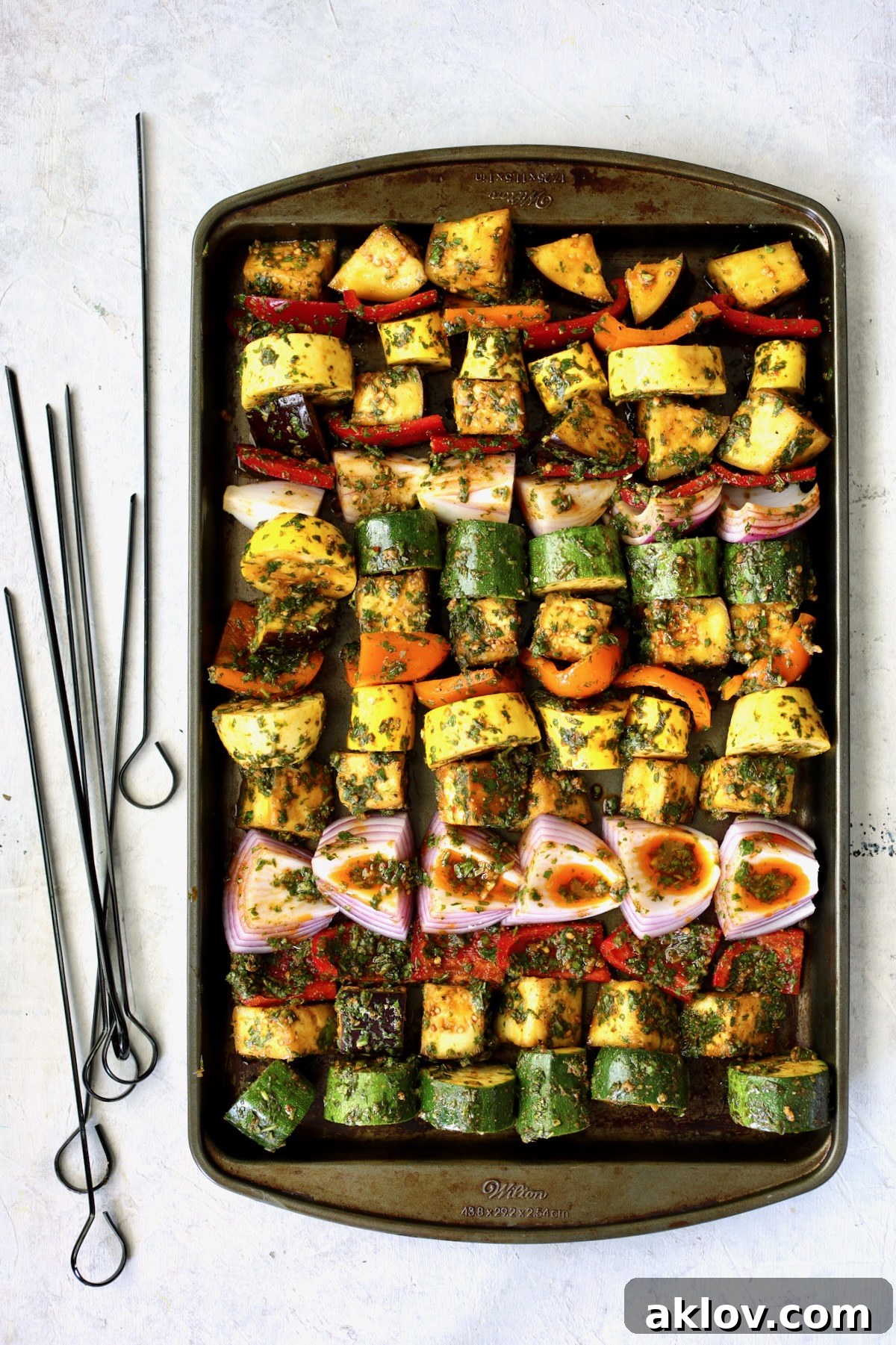 Marinated, cubed vegetables meticulously arranged on a rimmed sheet pan, precisely organized before being threaded onto skewers.
