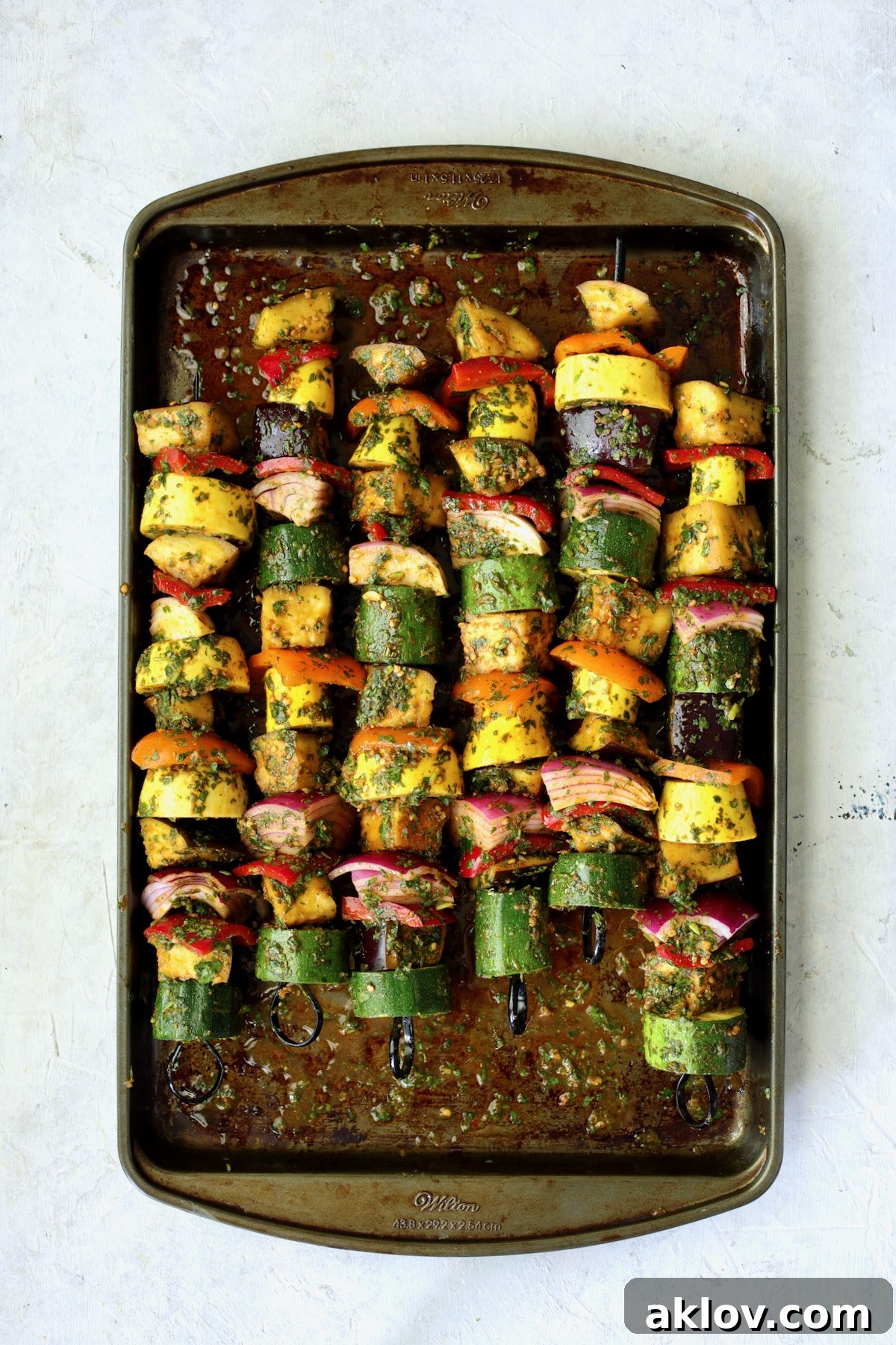 Beautifully threaded vegetable kabobs, coated in marinade, lined up on a sheet pan, ready for the grill.