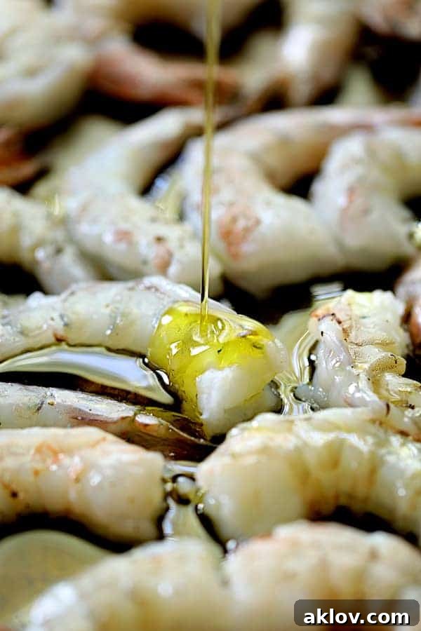 Photo of raw shrimp being drizzled with olive oil on baking sheet.