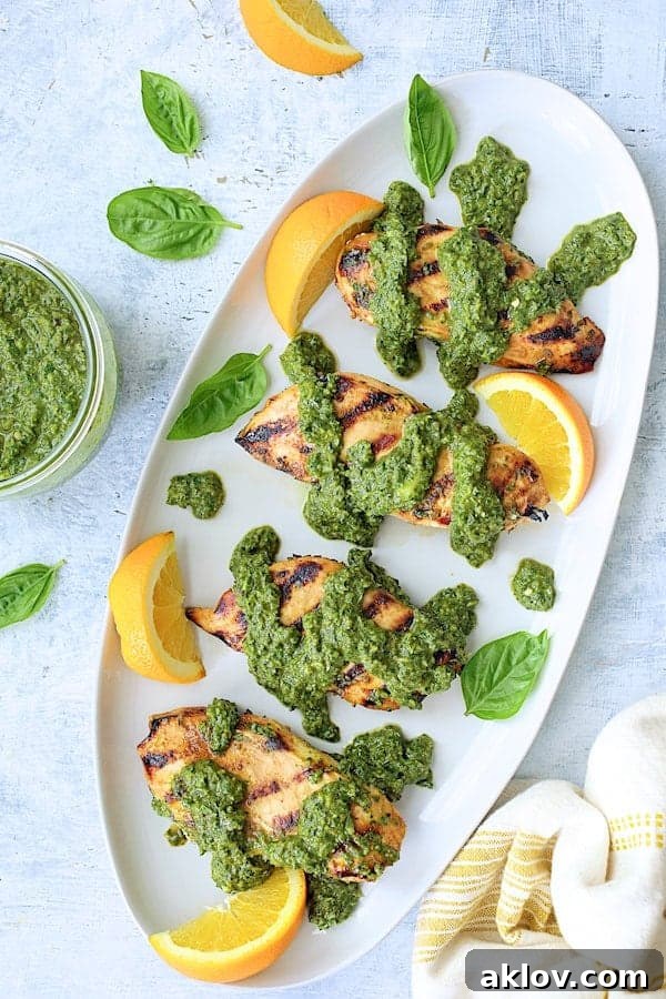 Photo of Grilled Citrus Chicken with Spicy Basil Chimichurri on white oval platter garnished with orange wedges and fresh basil leaves.