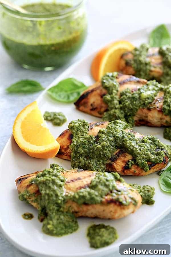 Close-up photo of Grilled Citrus Chicken with Spicy Basil Chimichurri Sauce on white serving platter garnished with orange wedges.