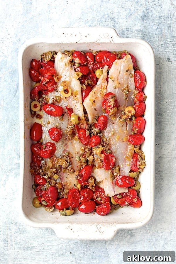 Photo of fish with tomato/olive combination before in white baking dish before being baked.