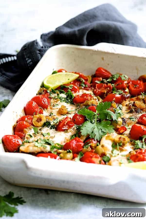 Close-up photo of Baked Veracruz-Style Fish (Pescado A La Veracruzana) in white baking dish with dark blue towel in the background.