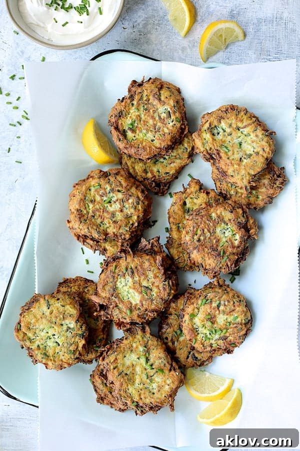 Crispy golden Zucchini Ricotta Fritters arranged neatly on parchment paper on a light blue tray, garnished with fresh lemon wedges, showcasing their appealing texture.
