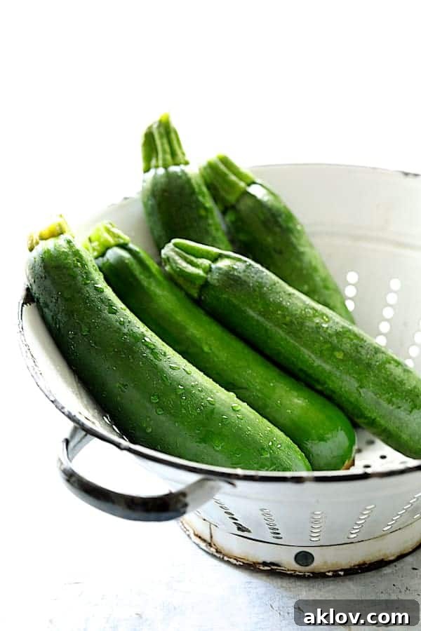 Five fresh green zucchini nestled in a white colander, ready for preparation.