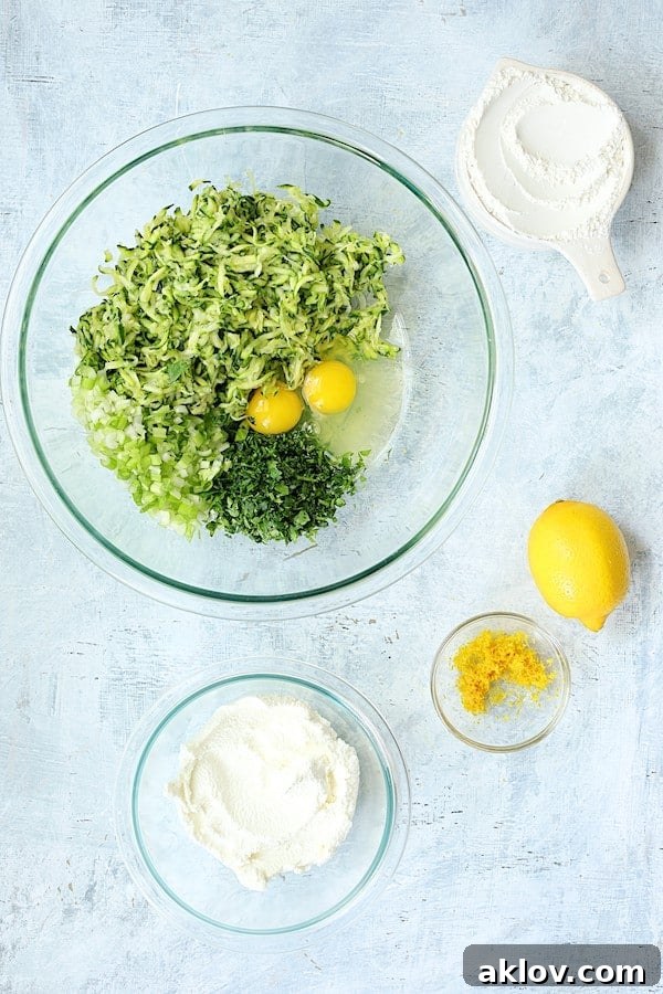 Various ingredients for Zucchini Ricotta Fritters, including shredded zucchini, ricotta, eggs, flour, and herbs, neatly arranged in glass bowls.
