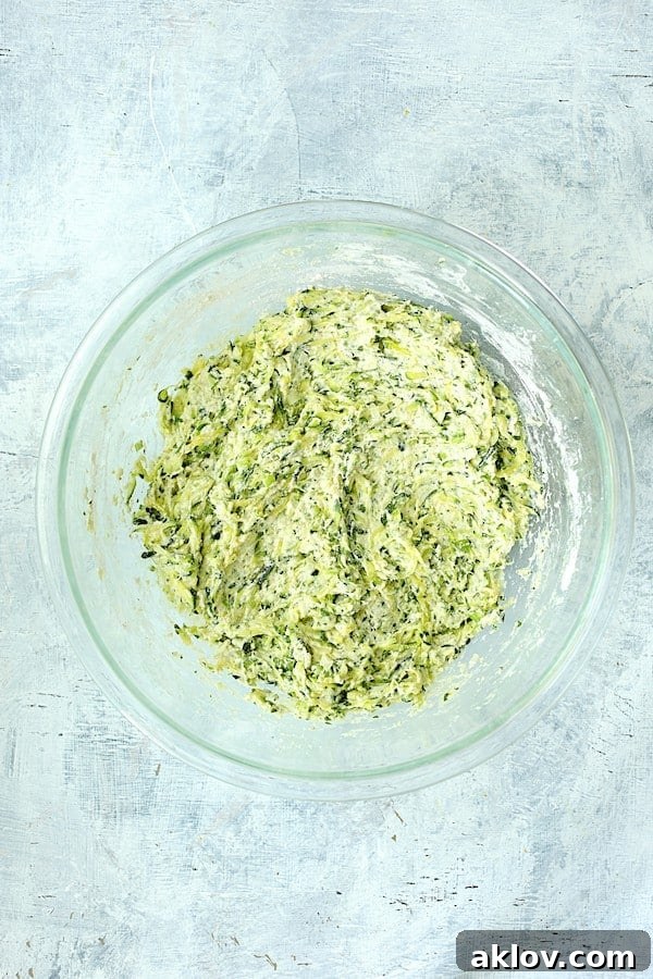 A glass mixing bowl containing the perfectly blended batter for Zucchini Ricotta Fritters, showcasing its ready-to-fry consistency.