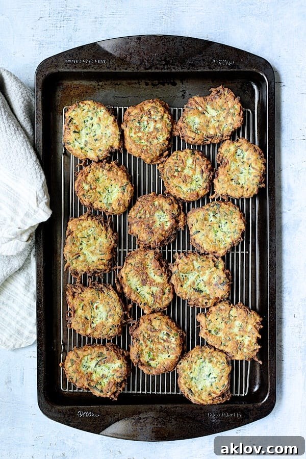 Freshly fried Zucchini Ricotta Fritters draining on a wire cooling rack placed over a baking sheet, ensuring optimal crispness.