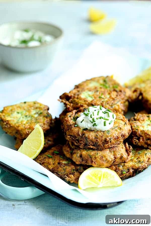 An appetizing display of Zucchini Ricotta Fritters arranged on a parchment paper-lined serving tray, elegantly garnished with fresh lemon.