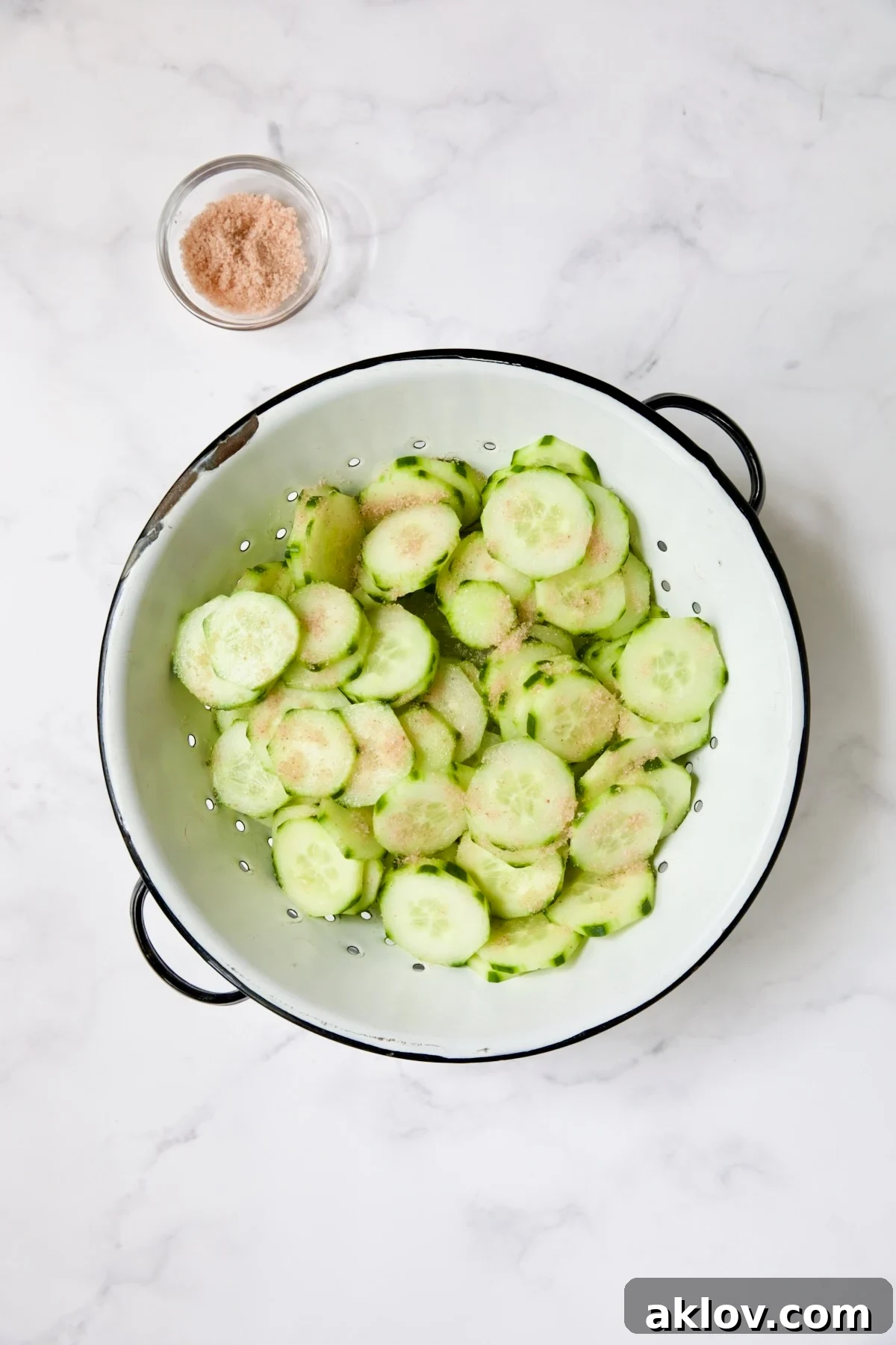 Cucumber in white distressed colander with salt sprinkled over them.