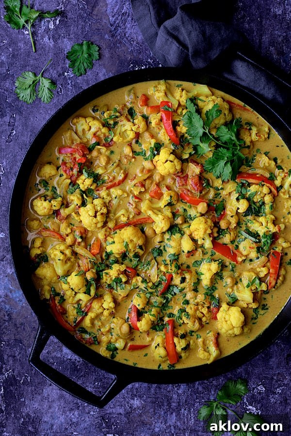 Close-up photo of vibrant Vegan Indian Cauliflower and Chickpea Curry in a rustic cast iron skillet, garnished with fresh cilantro, ready to be served.