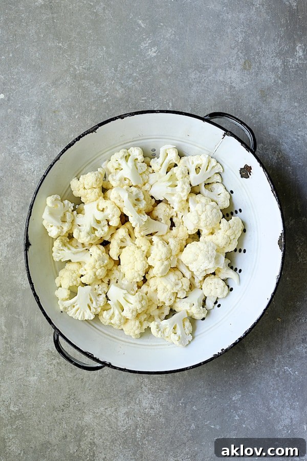 Golden Vegan Cauliflower Chickpea Curry 4 Fresh, raw cauliflower florets resting in a white distressed colander against a soft gray background, awaiting their transformation into a delicious curry.