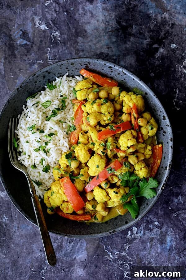 Photo of a serving of Vegan Indian Cauliflower and Chickpea Curry in a gray bowl, accompanied by fluffy basmati rice, showcasing a complete meal.