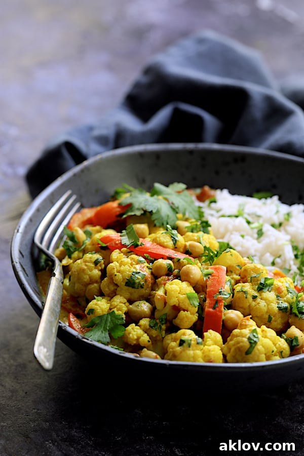 Photo of a single artfully plated serving of Vegan Indian Cauliflower and Chickpea Curry in a gray bowl, with basmati rice, emphasizing presentation.