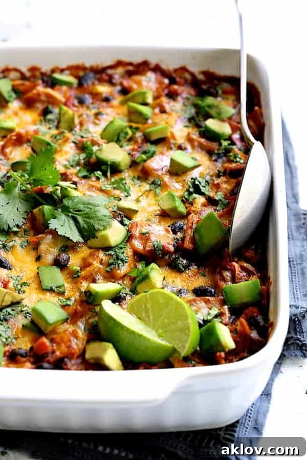 Photo of baked Black Bean and Yellow Squash Enchilada Casserole with serving spoon garnished with lime wedges and cilantro sprigs.