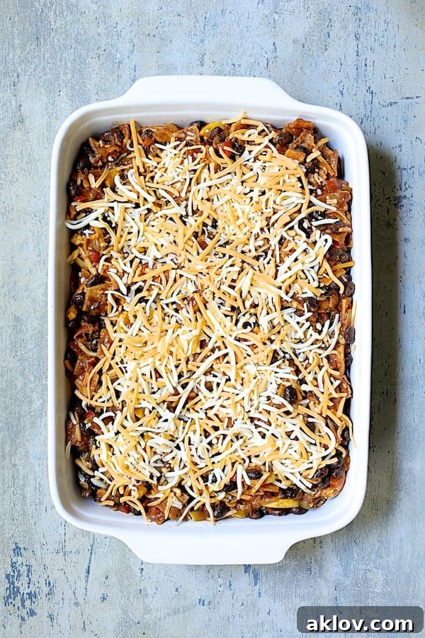 Photo of casserole in white baking dish with cheese added before being baked.