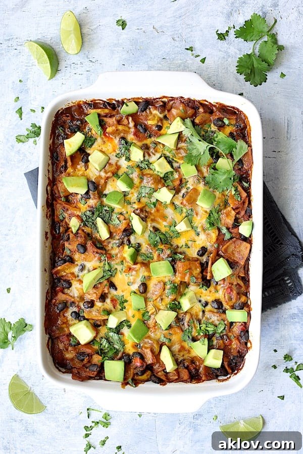 Photo of baked casserole in white baking dish garnished with cilantro, lime wedges and avocado.