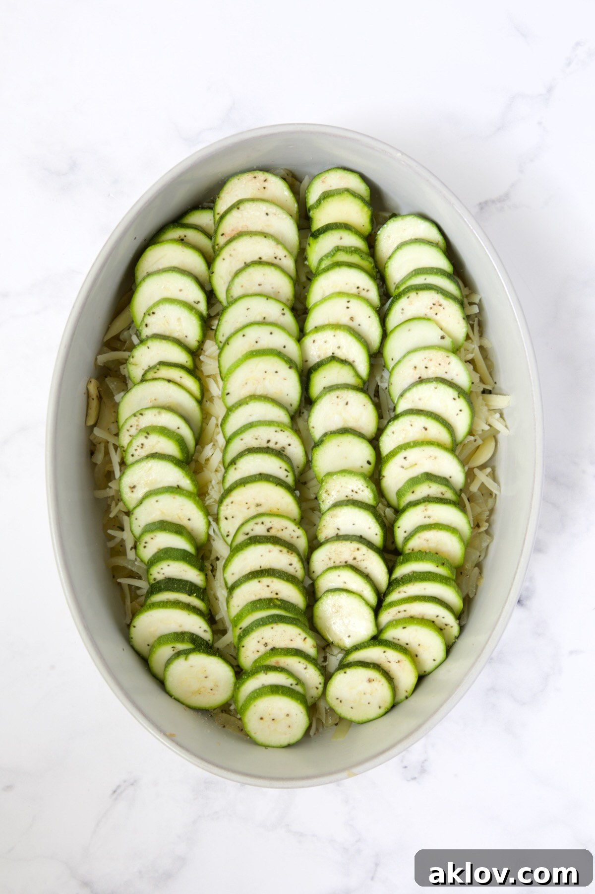 Sliced zucchini added to oval baking dish with the cheese and onion mixture.