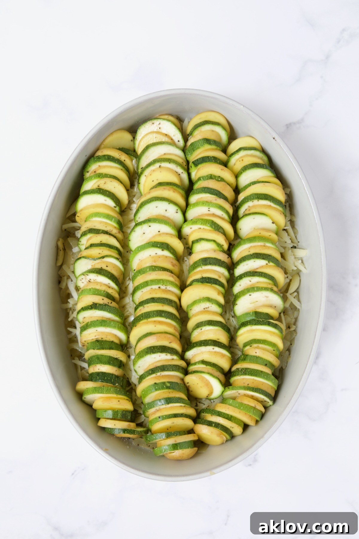Sliced potatoes and zucchini in oval baking dish.