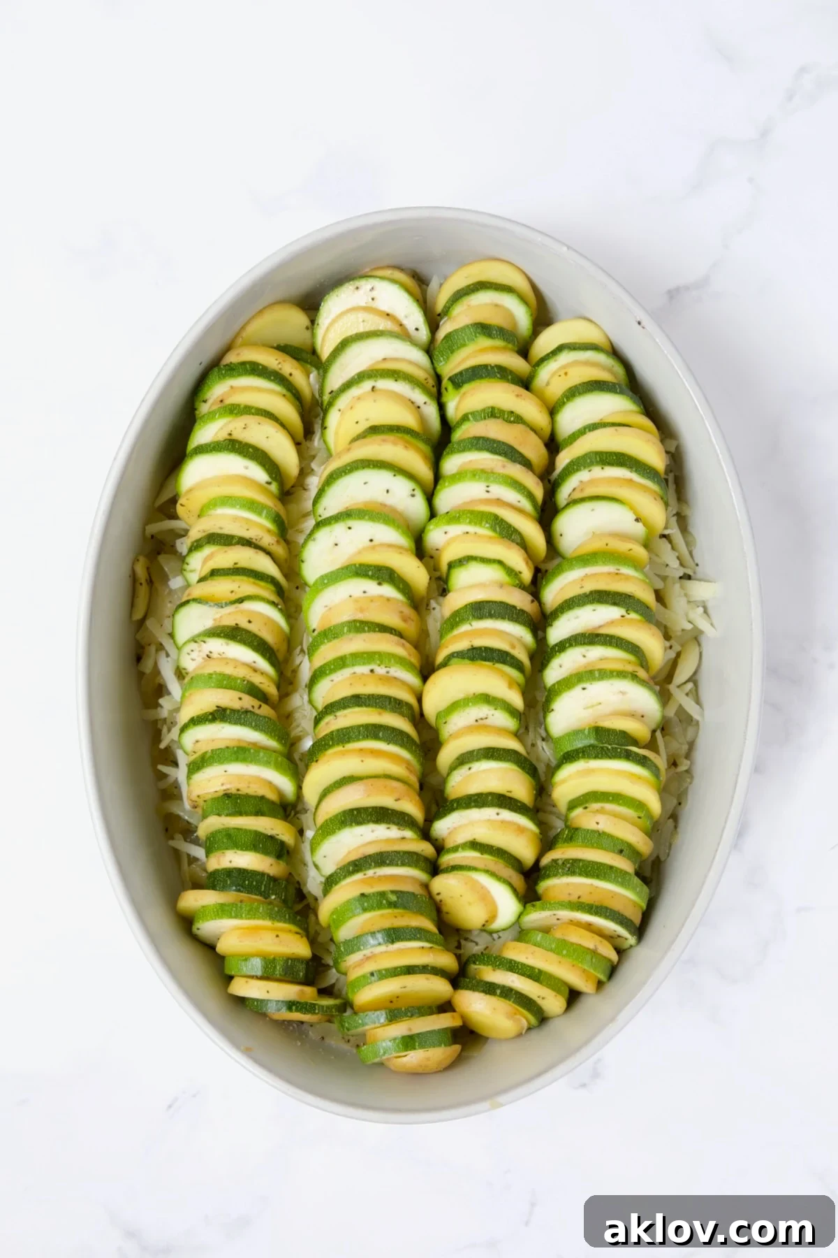 Alternating layers of sliced potatoes and zucchini arranged in the oval baking dish.