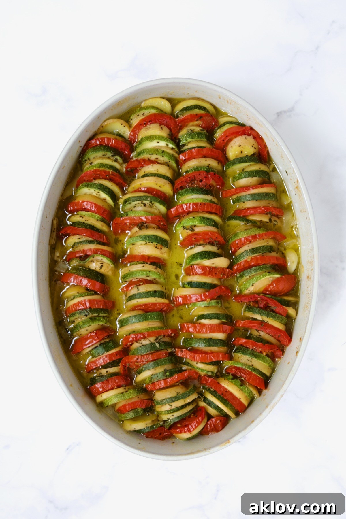 Baked zucchini, potatoes and tomatoes in oval baking dish.