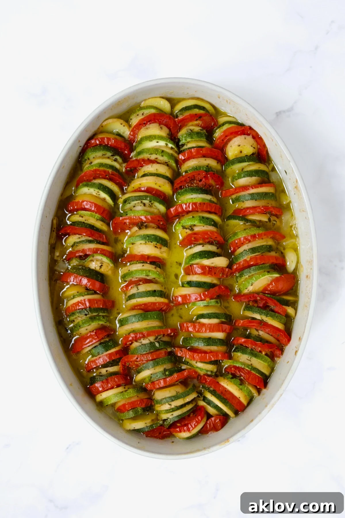 Baked zucchini, potatoes, and tomatoes in an oval baking dish after initial covered baking.