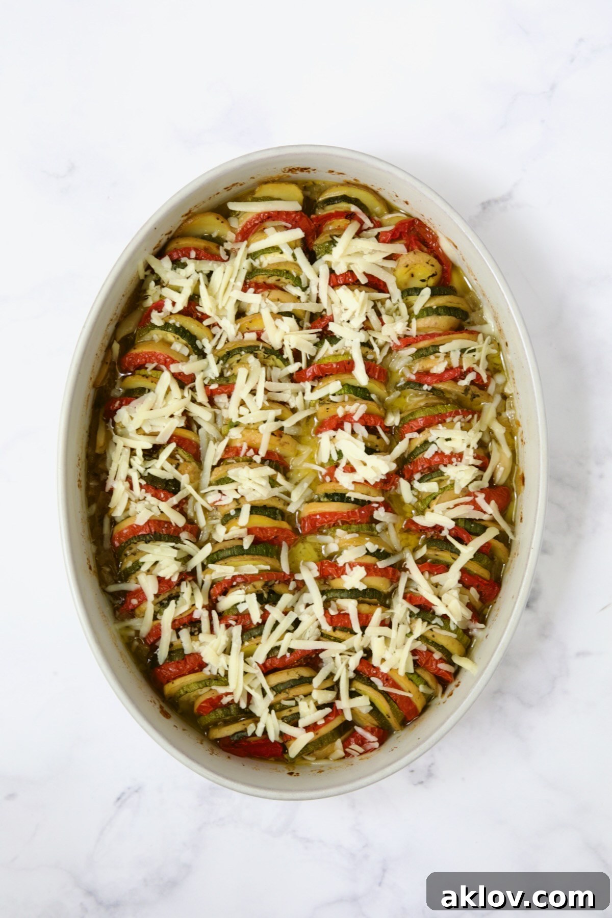 Cheese added to cooked vegetables in oval baking dish.
