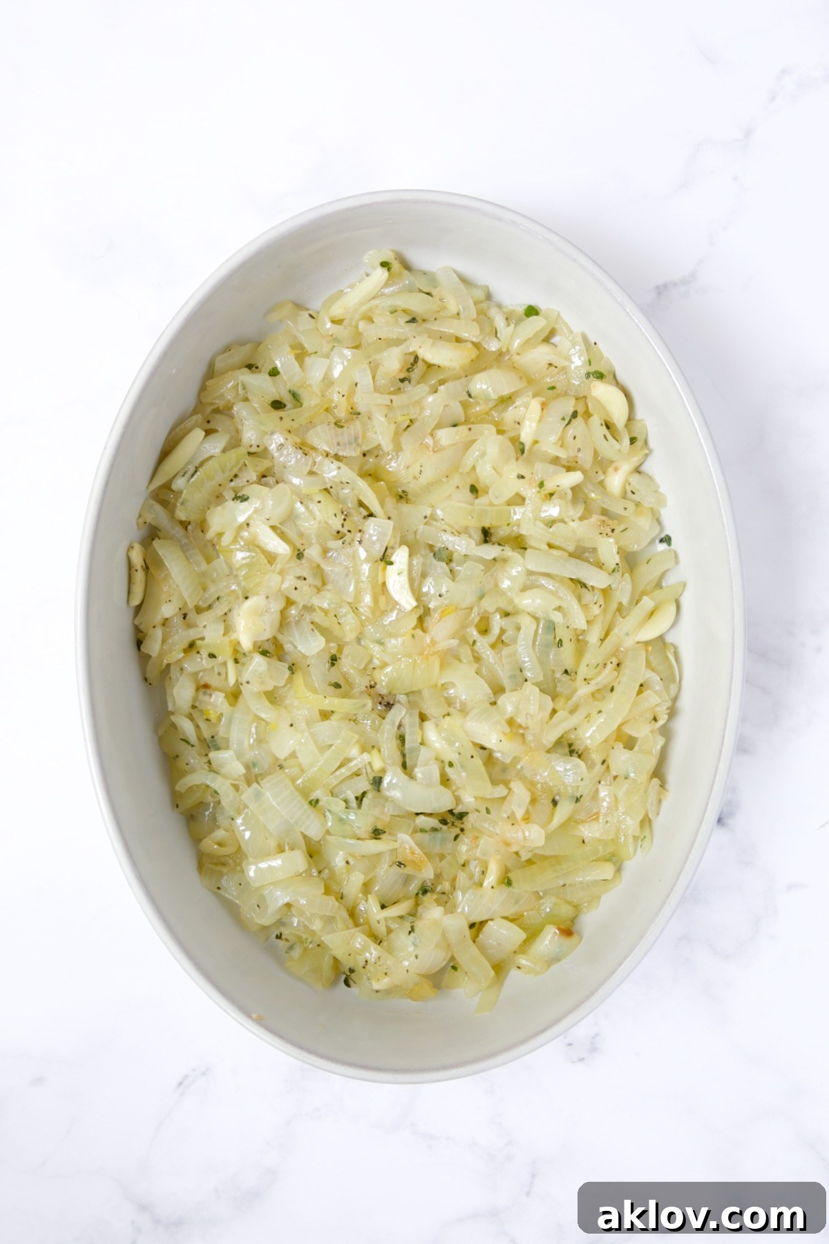 Onion, garlic and thyme mixture in oval baking dish.