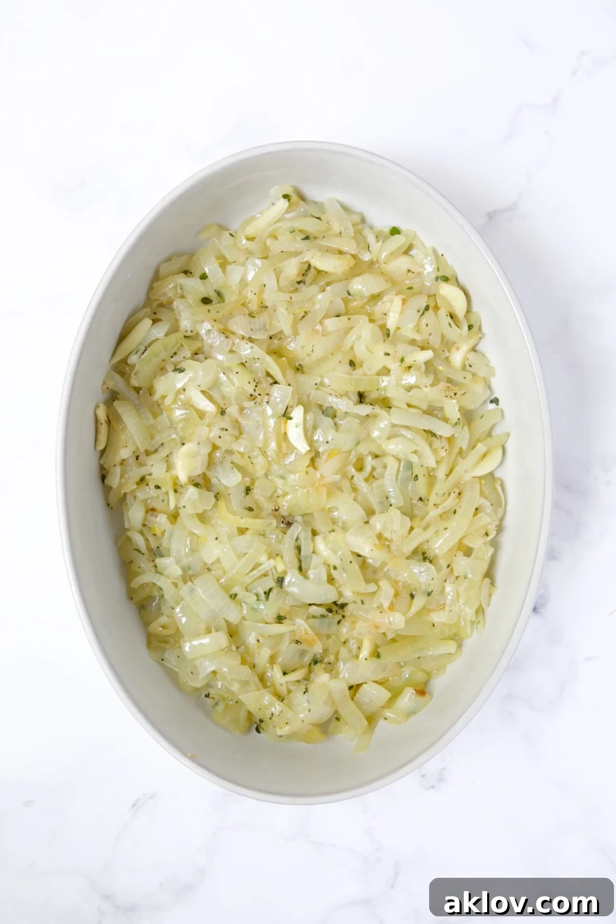 The cooled onion, garlic, and thyme mixture spread evenly in an oval baking dish.