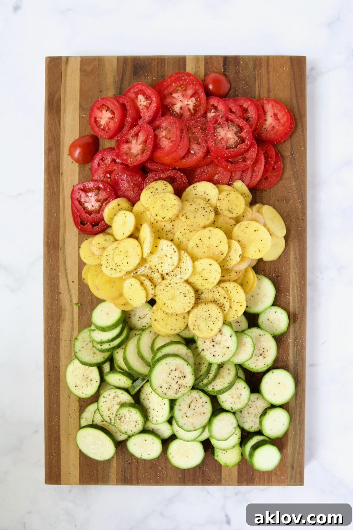 Sliced tomatoes, sliced Yukon Gold potatoes and sliced zucchini on wood cutting board.