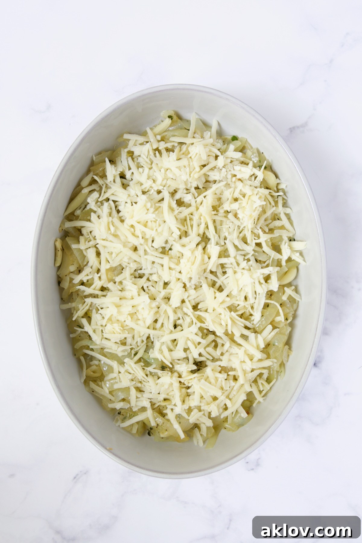 Cheese added to onion, garlic and thyme combination in oval baking dish.